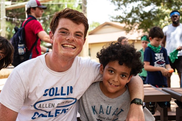 A camper and his counselor smile together at summer camp. 