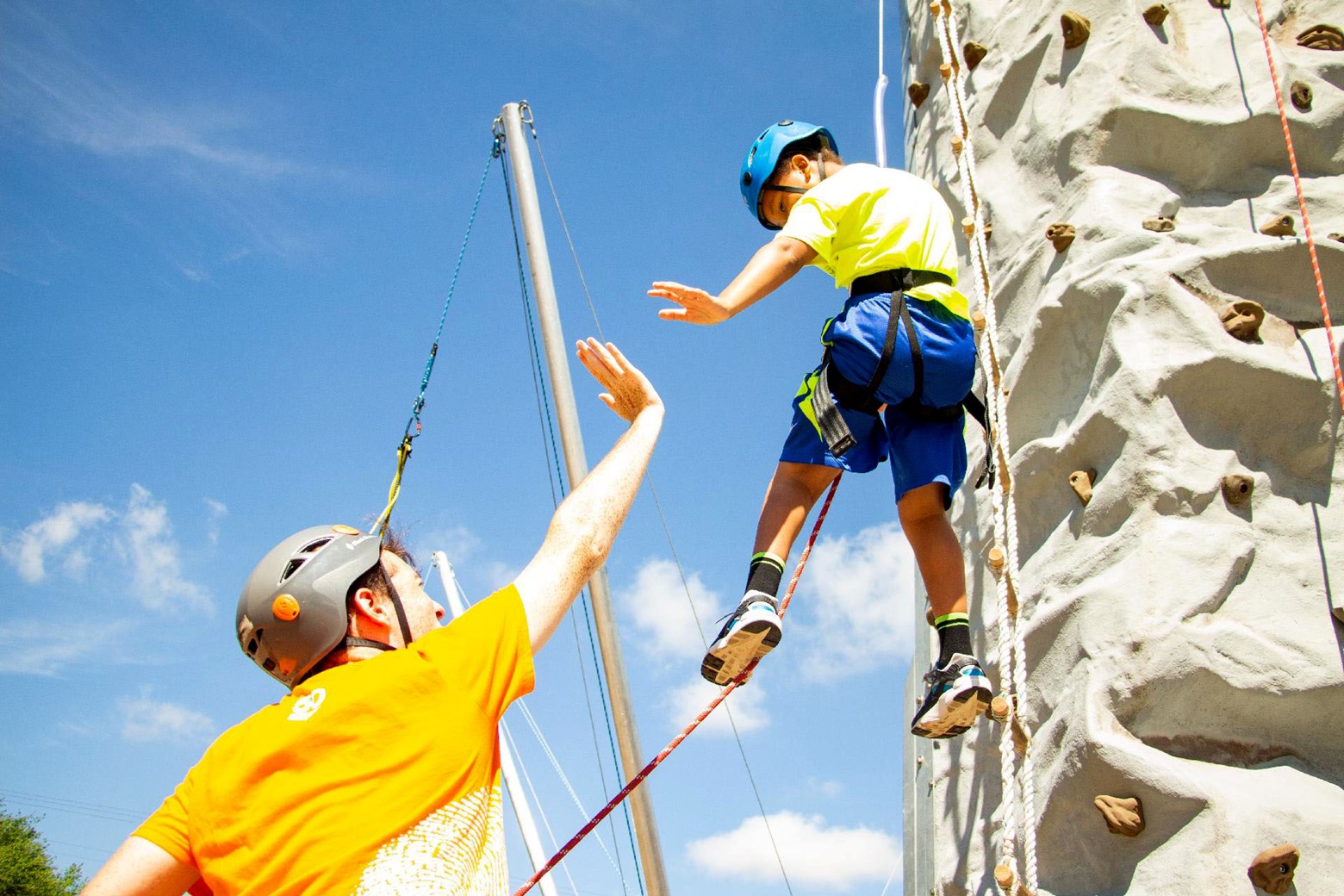 Why You Should Work at Camp at Least Once in Your Life photo of boy on climbing wall high-fiving camp staff